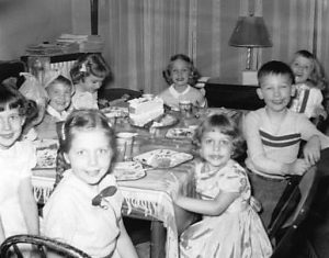 Birthday party 1954 for a five-year-old girl with children around a table and a birthday cake with candles